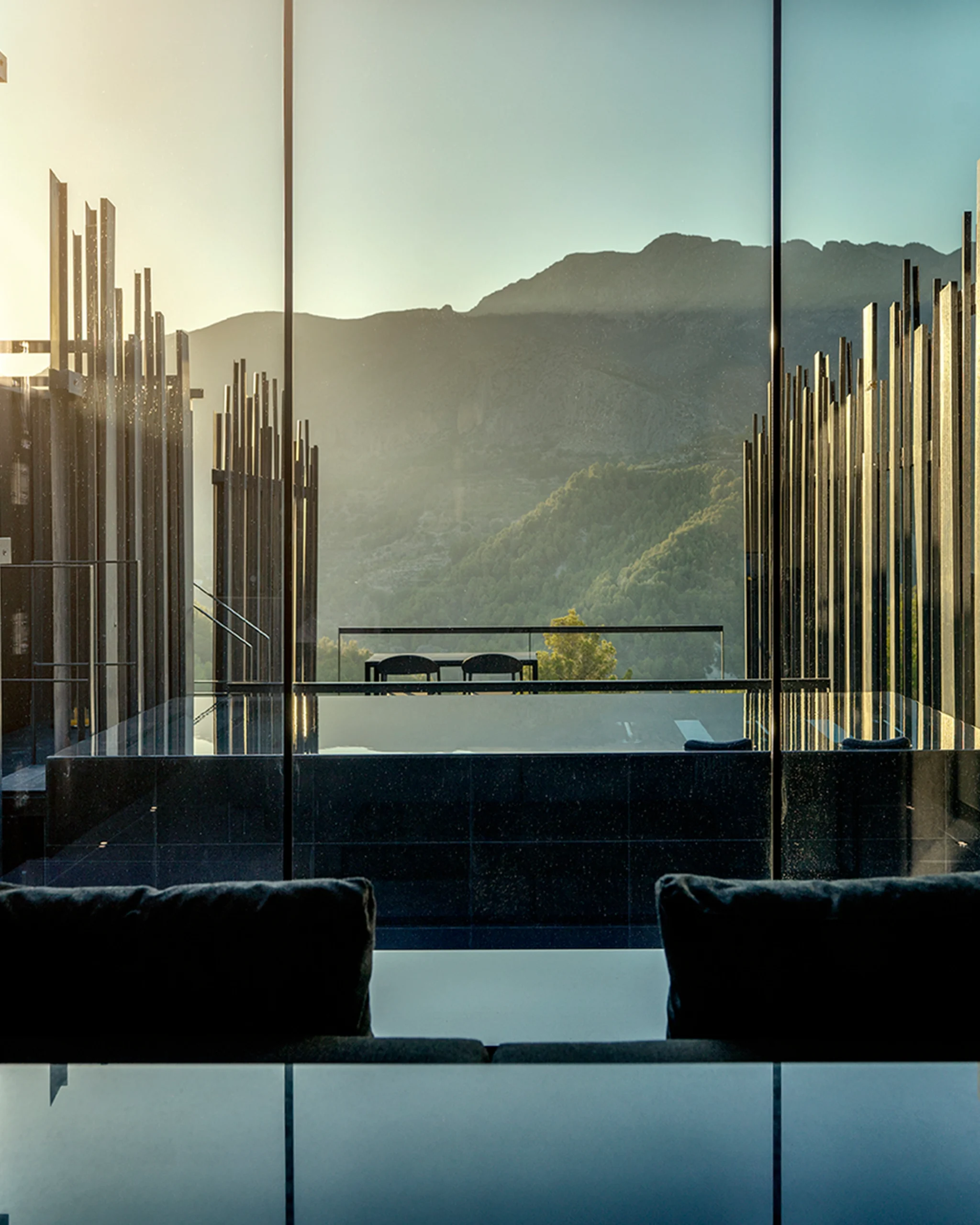 Vista desde el interior de una villa de lujo en Alicante al atardecer, con piscina privada y montaña al fondo.