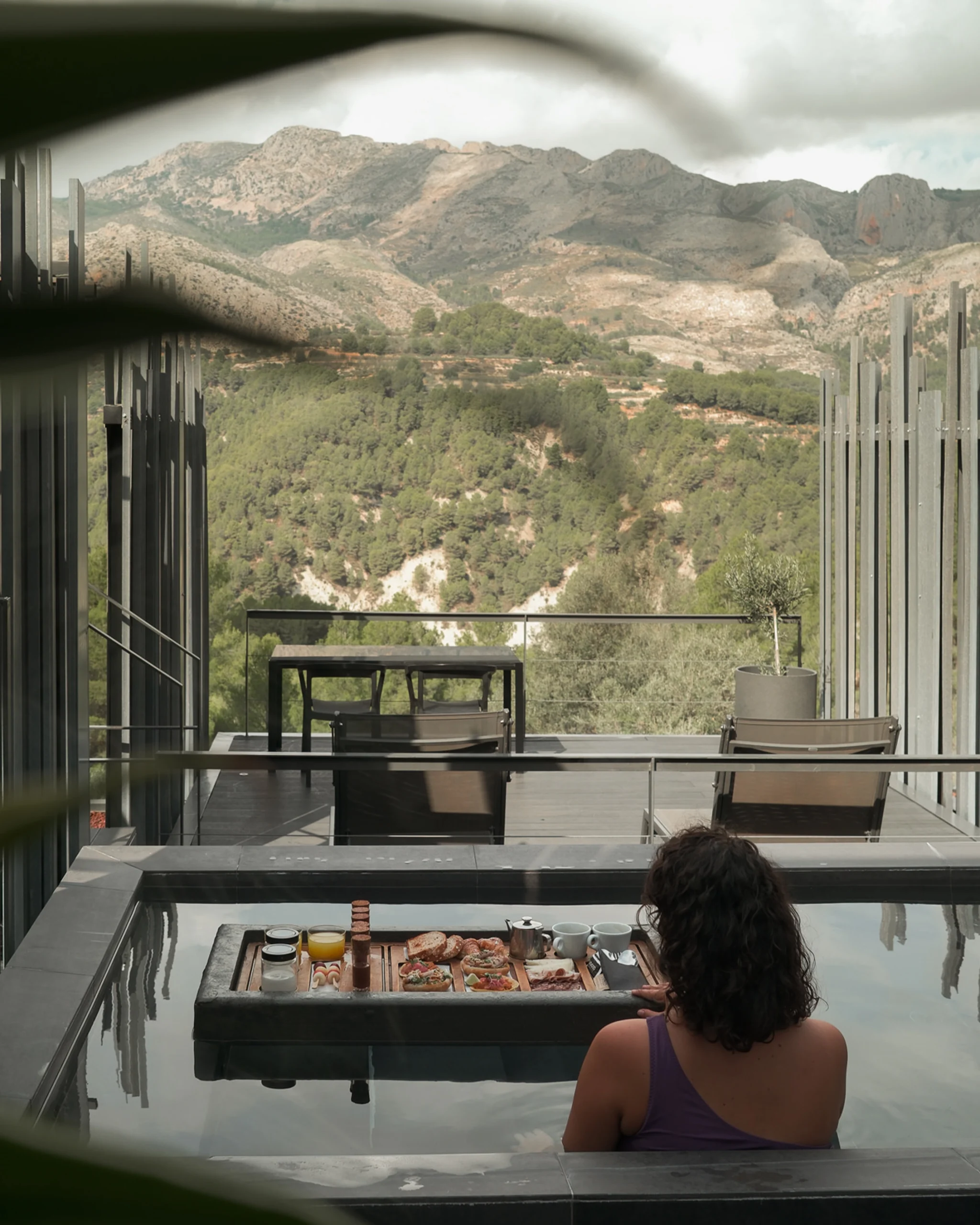 Mujer disfrutando de un desayuno flotante en piscina privada con vistas a la montaña en un hotel boutique de Alicante.