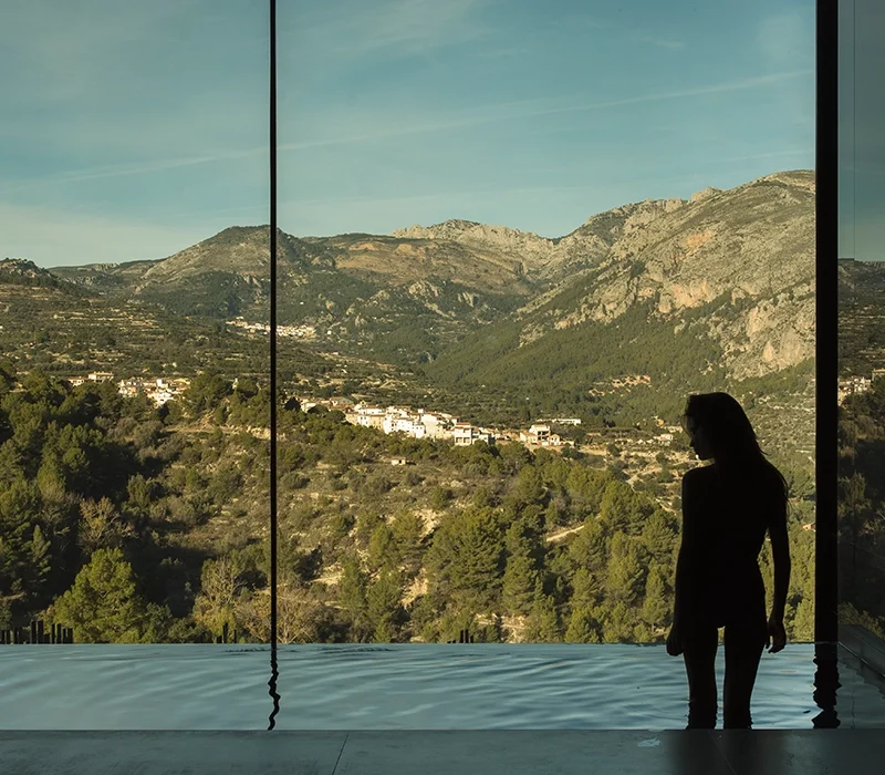 Mujer contemplando el paisaje de montaña desde la piscina climatizada de un hotel spa en Alicante