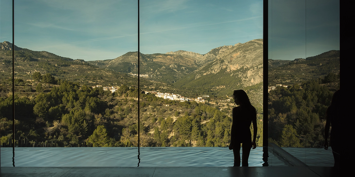 Mujer contemplando el paisaje de montaña desde la piscina climatizada de un hotel spa en Alicante