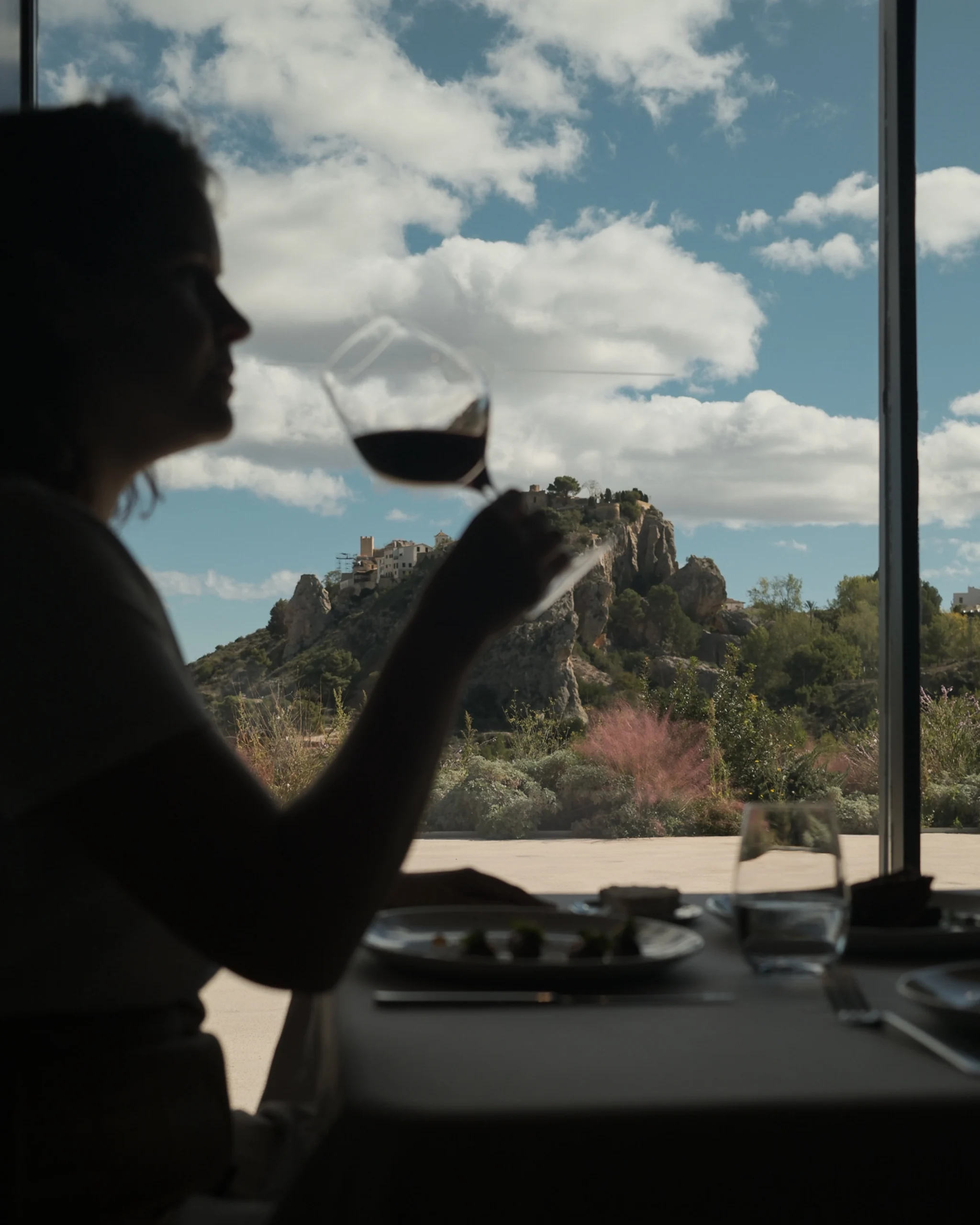 Mujer disfrutando de una copa de vino con vistas al castillo de Guadalest desde el restaurante de VIVOOD.