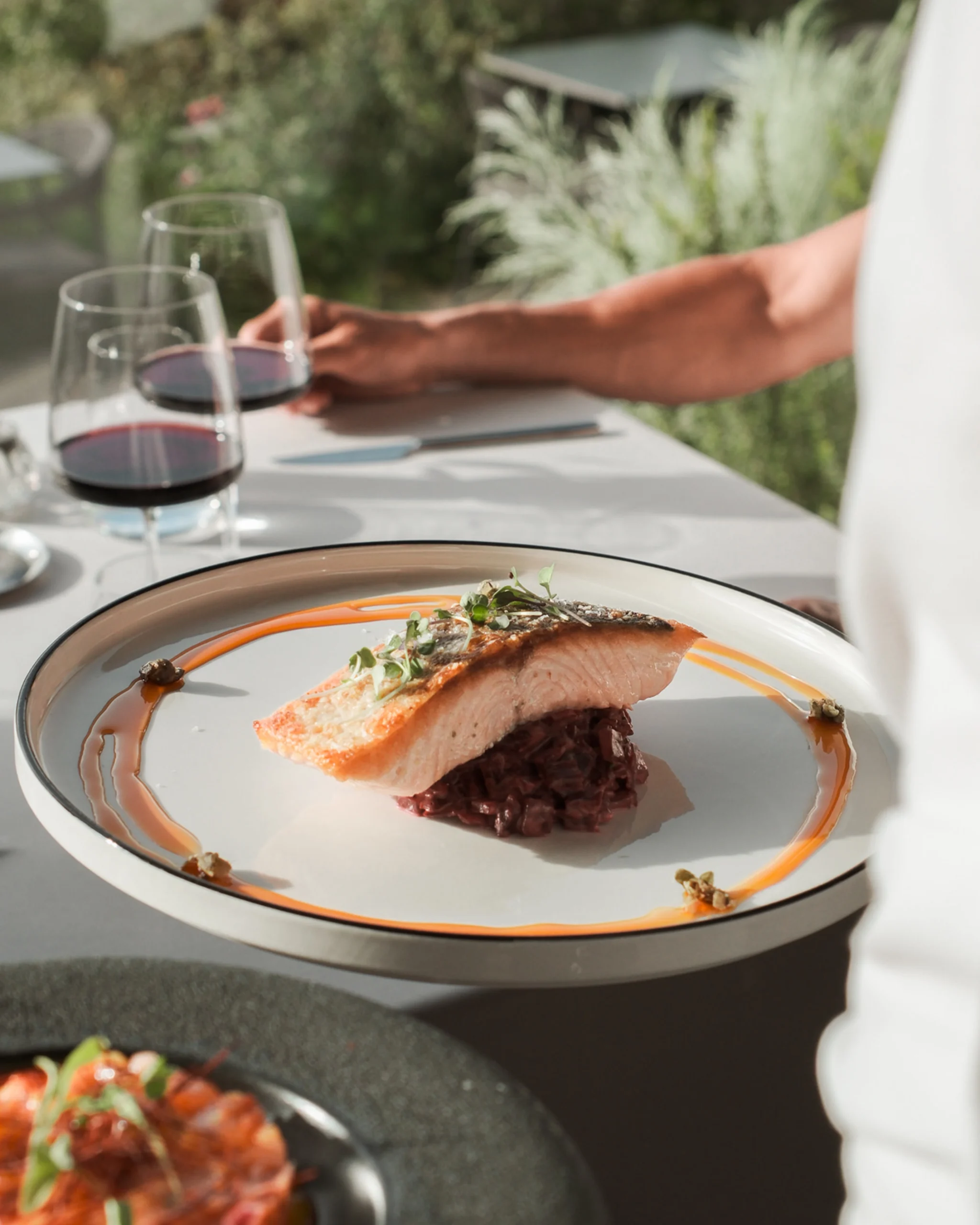 Salmón crujiente servido sobre arroz meloso en mesa con copas de vino tinto en VIVOOD.